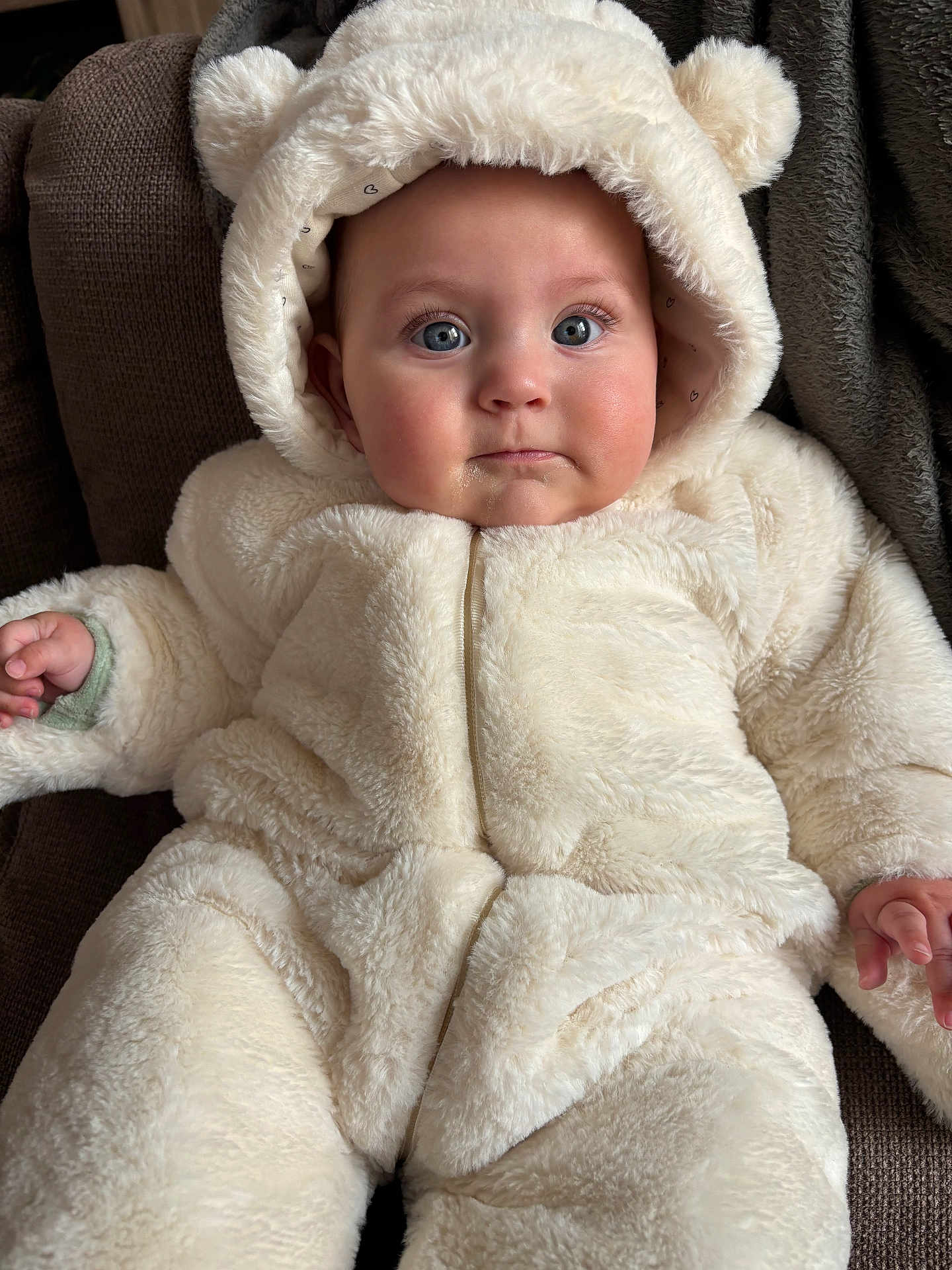 Adriana participe au concours pour gagner de l'argent avec cette photo : baby, child, infant, fluffy_suit, bear_ears, hood, blue_eyes, couch, soft_texture, cute, warm_clothing, indoor, portrait, face, hand, seated, cozy, expression, person, young_child