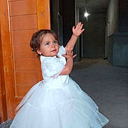 Souad participe au concours pour gagner de l'argent avec cette photo : child, toddler, white_dress, curly_hair, earrings, indoor, wooden_door, hallway, floor, concrete_wall, lighting, playful_pose, person, young_child, dress, cute, portrait, small_child, standing, looking_up