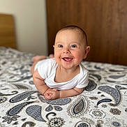 Darius participe au concours pour gagner de l'argent avec cette photo : baby, smiling, infant, bed, blanket, paisley_pattern, white_clothing, chubby_cheeks, happy, portrait, indoor, closeup, head, face, skin, cute, lying_down, person, child, expression