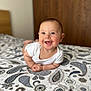 baby, smiling, infant, bed, blanket, paisley_pattern, white_clothing, chubby_cheeks, happy, portrait, indoor, closeup, head, face, skin, cute, lying_down, person, child, expression
