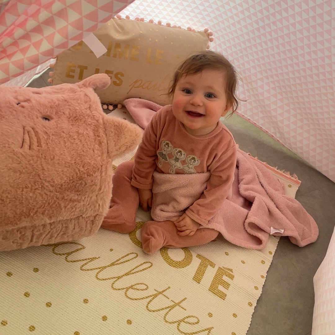 Fayza a rejoint le concours — aidez-le/la à gagner de superbes lots ! baby, blanket, carpet, child, clothing, cozy, cute, floor, happy, indoor, pattern, person, pillow, pink, plush_toy, sitting, smiling, soft, tent, toddler