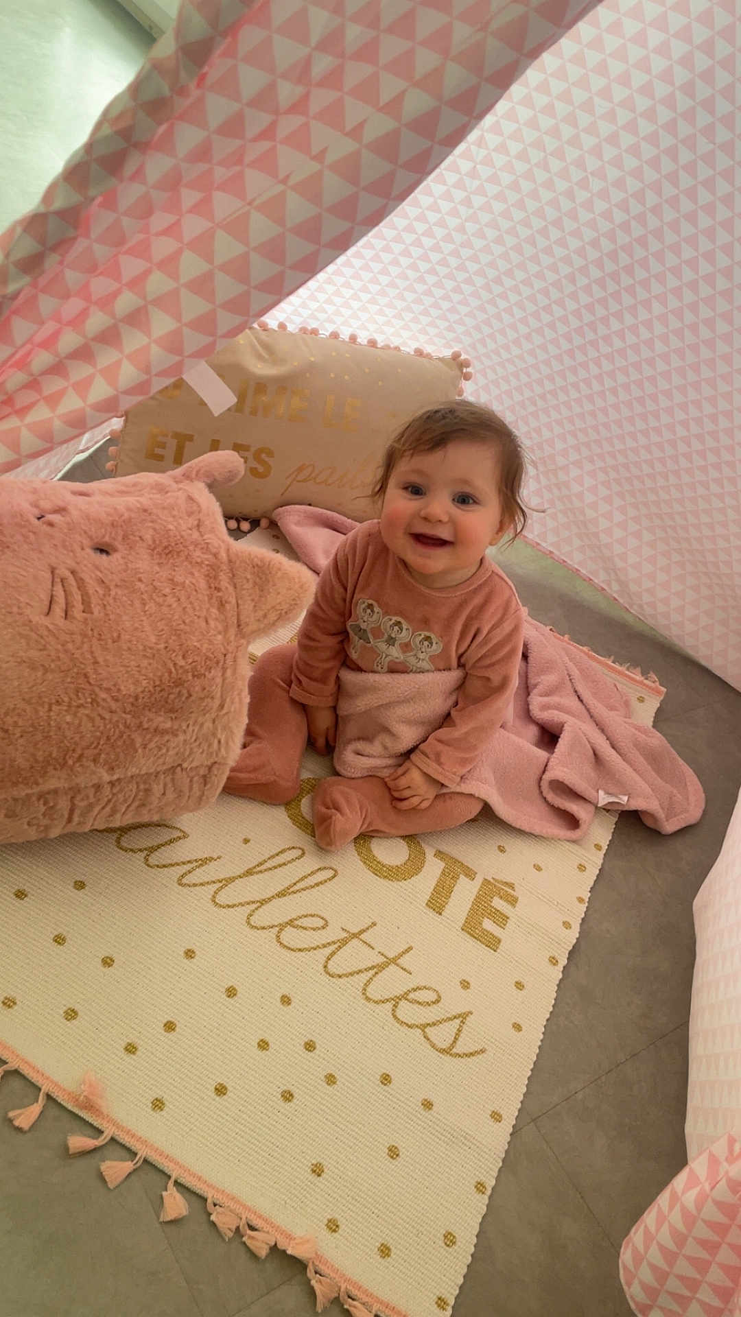 Fayza a rejoint le concours — aidez-le/la à gagner de superbes lots ! baby, child, smiling, indoor, tent, blanket, plush_toy, pillow, carpet, pink, pattern, floor, cute, happy, sitting, cozy, soft, toddler, clothing, person