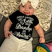 Adalynn is registered to the contest to win money with this photo: baby, infant, smile, face, headwear, bow, shirt, text, blanket, fur, pajamas, lying_down, hand, cute, child, cozy, indoor, person, soft, colorful
