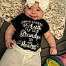 baby, infant, smile, face, headwear, bow, shirt, text, blanket, fur, pajamas, lying_down, hand, cute, child, cozy, indoor, person, soft, colorful