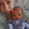 Meridith is registered to the contest to win money with this photo: baby, newborn, woman, selfie, bed, hospital_gown, purple_onesie, face, portrait, doodle, red_horns, lying_down, closeup, skin, person, cute, tender_moment, indoor, soft_light, family