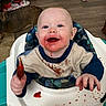baby, high_chair, messy, food, spoon, smiling, face, shirt, red_sauce, floor, dog, happy, indoor, child, feeding, wooden_floor, toy, cute, person, home