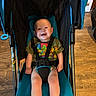 baby, smiling, toddler, stroller, safety_harness, tshirt, green_clothing, wooden_floor, indoor, child, happy, seat, person, cute, infant, legs, face, head, sitting, bright