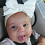 baby, infant, child, car_seat, white_bow, headband, tongue_out, smiling, close_up, safety_strap, cute, happy, person, seatbelt, indoors, warning_label, skin, face, expression, apparel