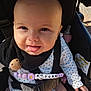 baby, child, stroller, pacifier_clip, black_bib, smiling, tongue_out, sunlight, floral_outfit, seatbelt, infant, cute, portrait, closeup, outdoor, happy, face, hand, bottle, safety