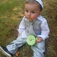 Everett joined the competition — help win amazing prizes! child, baby, grass, outdoor, sitting, formal_clothing, suit, tie, shirt, cup, green_cup, headwear, boy, curious_expression, nature, daylight, shoes, young_child, person, casual_pose