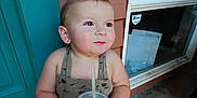 Everett is registered to the contest to win money with this photo: toddler, child, drink, cup, straw, romper, dinosaur_print, smile, outdoor, door, window, concrete, shoes, cute, person, young_child, holding, happy, casual, daylight