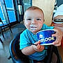 Everett is registered to the contest to win money with this photo: toddler, child, high_chair, ice_cream, milk_mustache, blue_shirt, cup, spoon, indoor, restaurant, wooden_pillar, floor, chair, table, person, smile, happy, casual, food, eating