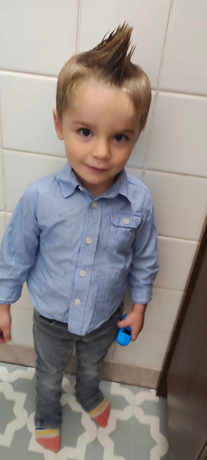 Maël participe au concours pour gagner de l'argent avec cette photo : child, boy, blue_shirt, jeans, toy_car, mohawk_hairstyle, indoor, floor_tiles, patterned_floor, socks, casual, standing, portrait, young, person, smile, hair, clothing, playful, holding