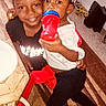 Devon is registered to the contest to win money with this photo: children, siblings, toddler, smiling, portrait, indoor, toy, bottle, red_toy, blue_toy, braids, hair_bows, black_clothing, white_shirt, black_pants, carpet, rug, chair, table, playtime