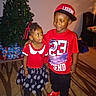 boy, child, children, christmas, christmas_tree, family, girl, hat, holiday, indoors, living_room, polka_dots, portrait, presents, red_clothing, skirt, smiling, standing, t_shirt, toddler