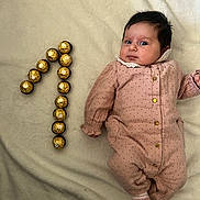 Zina participe au concours pour gagner de l'argent avec cette photo : baby, infant, blanket, clothing, onesie, polka_dot, gold_chocolate, number_one, celebration, soft_texture, lying_down, cute, face, head, expression, pink, beige, small_person, sweet, cozy