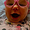 baby, child, glasses, headband, bow, smiling, laughing, selfie, portrait, pink, clothing, face, happy, infant, phone_screen, notification, text_message, patterned_clothing, indoors, closeup