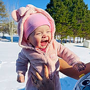Lauren joined the competition — help win amazing prizes! baby, child, pink_clothing, hat, hood, outdoor, snow, winter, tree, smiling, happy, person, hand, sunlight, forest, nature, cute, cold, joyful, playful
