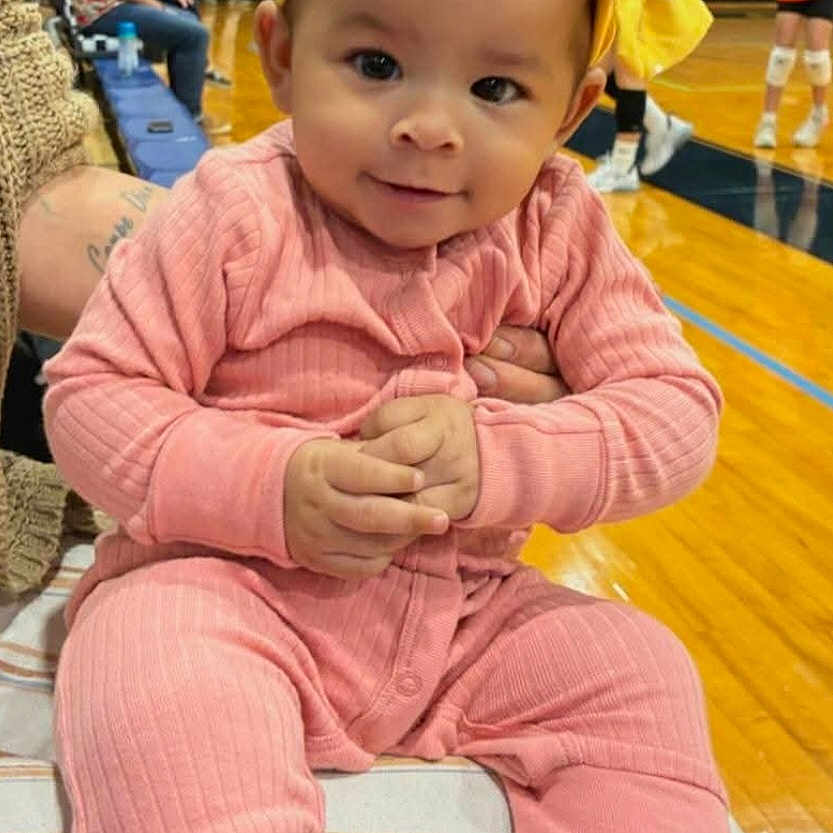 Skye joined the competition — help win amazing prizes! baby, child, pink_outfit, yellow_bow, headband, smile, hands, gymnasium, wooden_floor, people, background, seated, cushion, indoor, casual_clothing, curious_expression, infant, portrait, colorful, young_child