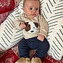 baby, infant, sweater, puppy_face, cushion, pillow, red_patterned_fabric, navy_pants, slippers, indoor, child, cute, comfortable, seated, looking_away, cozy, soft_toys, home, portrait, small_hands