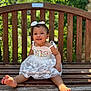 child, toddler, smiling, dress, white_dress, bow, headband, barefoot, bench, wooden_bench, outdoor, sunlight, greenery, happy, cute, portrait, baby, person, summer, nature
