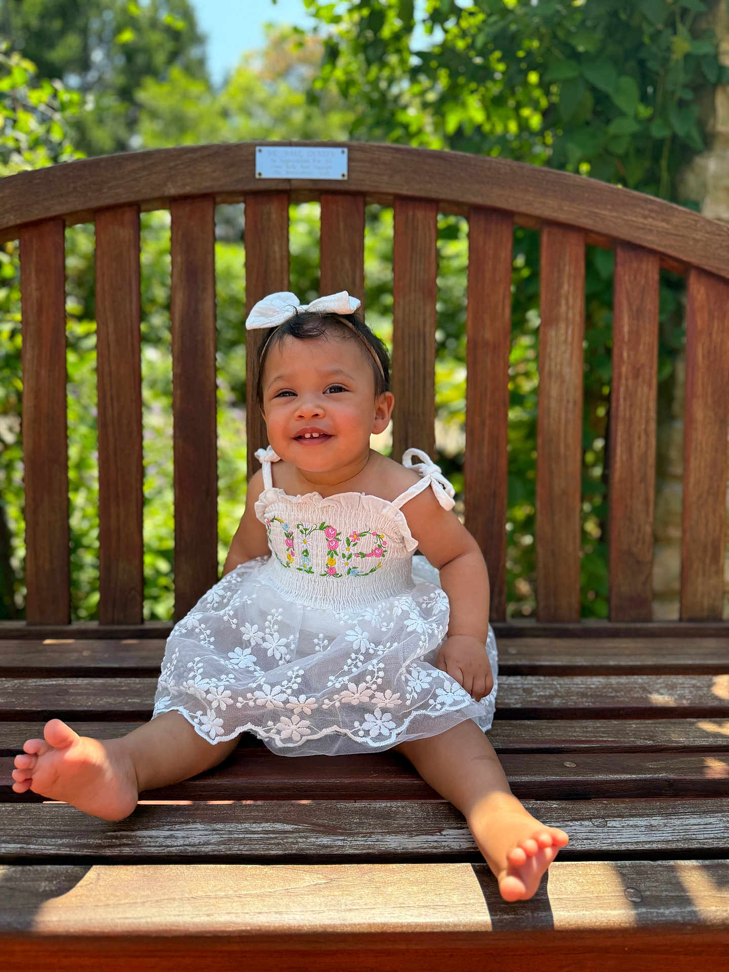 Violet joined the competition — help win amazing prizes! child, toddler, smiling, dress, white_dress, bow, headband, barefoot, bench, wooden_bench, outdoor, sunlight, greenery, happy, cute, portrait, baby, person, summer, nature