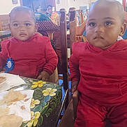 Aiden And Caden is registered to the contest to win money with this photo: toddler, child, red_clothing, table, food, restaurant, chair, indoor, face, person, baby, decorations, napkin, chips, wooden_furniture, expressionless, seated, colorful, celebration, family