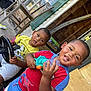Aiden And Caden is registered to the contest to win money with this photo: child, boy, smiling, toy, porch, outdoor, play, steering_wheel, water_toy, clothing, red_shirt, yellow_shirt, shorts, wood, door, window, chair, green_shutter, happy, casual