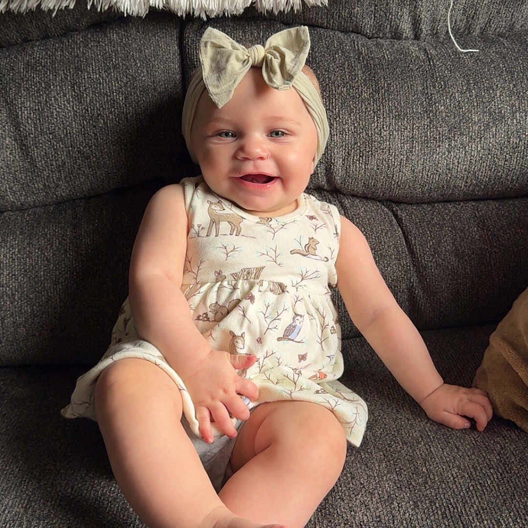 Ridgley is registered to the contest to win money with this photo: baby, bow, child, comfort, couch, cute, dress, face, foot, furniture, hand, happy, headband, home, indoor, infant, person, sitting, skin, smiling