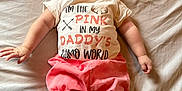 Ridgley is registered to the contest to win money with this photo: baby, infant, child, bed, headband, pink_shorts, shirt, text_on_shirt, arms, legs, face, expression, lying_down, soft_lighting, indoors, clothing, cute, adorable, skin, fabric