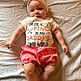 baby, infant, child, bed, headband, pink_shorts, shirt, text_on_shirt, arms, legs, face, expression, lying_down, soft_lighting, indoors, clothing, cute, adorable, skin, fabric