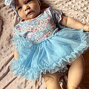 Ridgley is registered to the contest to win money with this photo: baby, infant, child, blue_tutu, headband, bow, floral_pattern, blanket, soft_texture, cute, portrait, lying_down, clothing, apparel, skin, face, legs, expression, indoors, person