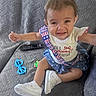 Raven is registered to the contest to win money with this photo: baby, child, couch, crying, dress, face, fashion, gray_background, indoors, infant, outstretched_arms, photography, portrait, remote_control, sitting, sneakers, stars, stripes, teary_eyes, toys