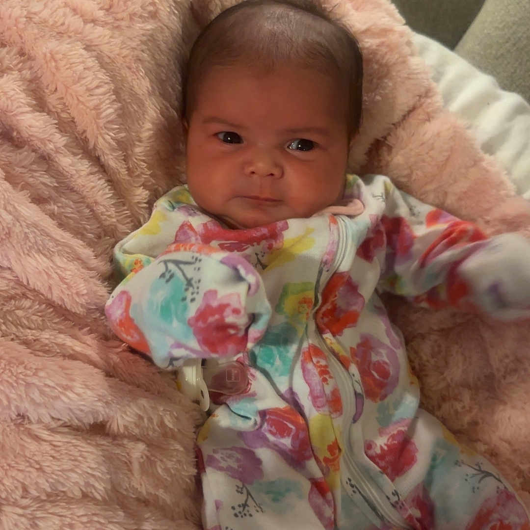 Raven is registered to the contest to win money with this photo: baby, blanket, child, colorful_clothing, comfort, couch, cute, expression, face, fluffy, indoor, infant, newborn, onesie, portrait, resting, seated, small_person, soft_texture, warm