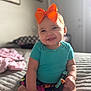 baby, bed, blanket, child, cute, furniture, hand_holding, happy, headband, home, indoor, infant, orange_bow, person, portrait, skin, skirt, smile, soft_light, teal_shirt