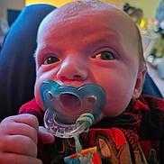 Kristopher is registered to the contest to win money with this photo: baby, pacifier, close_up, infant, indoor, child, face, hand, clothing, colorful, curious, portrait, soft_lighting, background_blur, cute, young_child, human, skin, expression, warm_colors