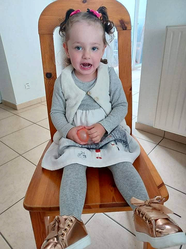 Lola a rejoint le concours — aidez-le/la à gagner de superbes lots ! baby, baby_products, baby_toddler_clothing, chair, comfort, dress, face, fashion_accessory, happy, head, human_leg, knee, lap, leg, person, sleeve, smile, sock, thigh, toddler
