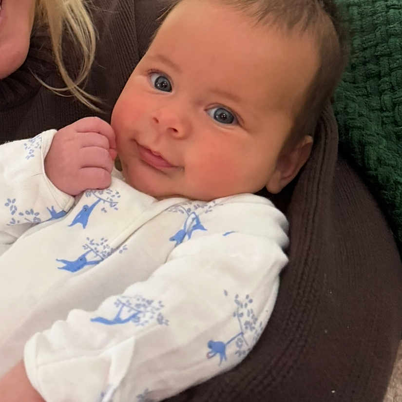 Callum joined the competition — help win amazing prizes! adorable, adult_partial, baby, blanket, blue_pattern, child, couch, cozy, cuddle, eyes, face, hair, hand, indoor, infant, knit_blanket, onesie, portrait, skin, smiling