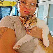 Jenny Falgoust is registered to the contest to win money with this photo: person, cat, indoor, glasses, tattoo, holding, pet, smile, kitchen, cabinet, furniture, short_sleeve_shirt, domestic_cat, fur, whiskers, ring, window, curtains, light, home