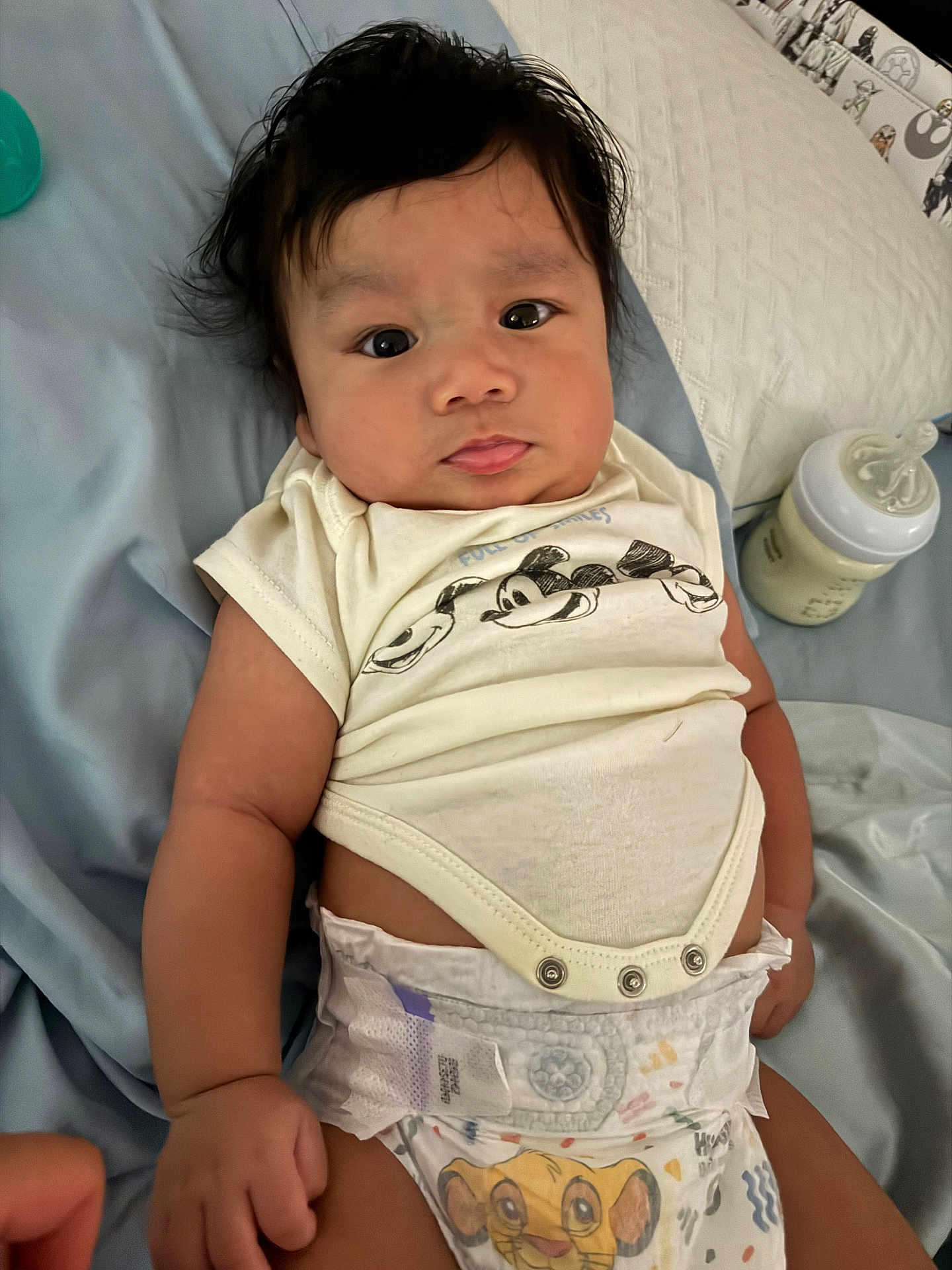 Kairo is registered to the contest to win money with this photo: baby, infant, diaper, mickey_mouse, simba, milk_bottle, bed, blanket, clothing, cute, person, face, hair, lying_down, indoors, child, skin, expression, hand, toddler