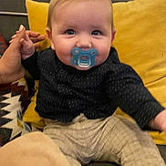 Nolan a rejoint le concours — aidez-le/la à gagner de superbes lots ! baby, pacifier, child, couch, hand, pillow, clothing, indoor, person, infant, sitting, cute, young_child, patterned_pants, smiling_eyes, holding_hand, yellow_pillow, dark_shirt, home, cozy