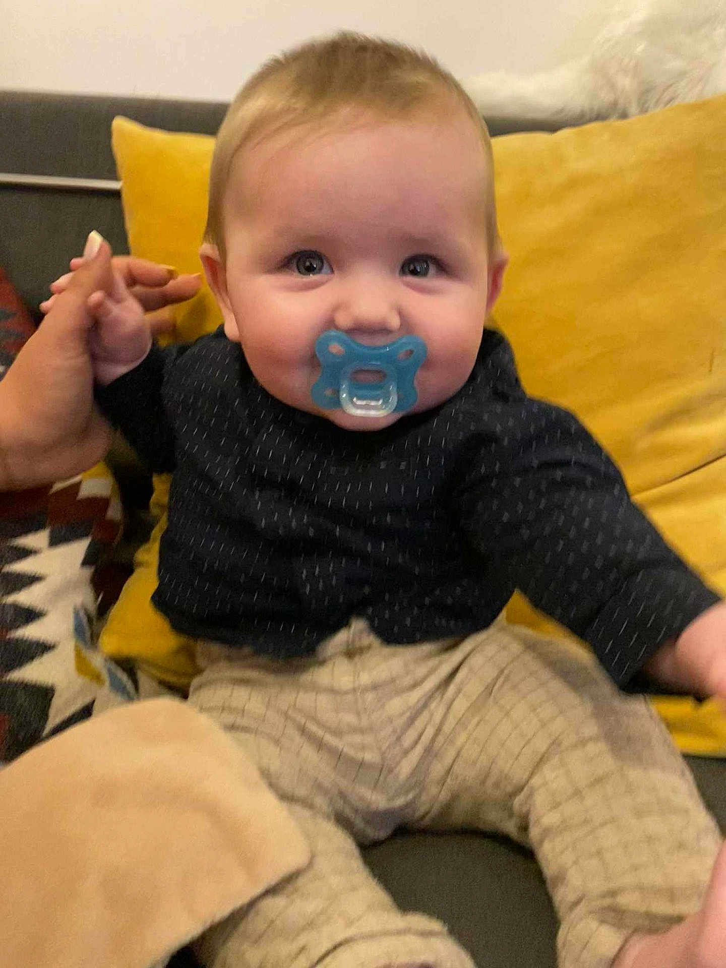 Nolan a rejoint le concours — aidez-le/la à gagner de superbes lots ! baby, pacifier, child, couch, hand, pillow, clothing, indoor, person, infant, sitting, cute, young_child, patterned_pants, smiling_eyes, holding_hand, yellow_pillow, dark_shirt, home, cozy