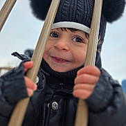 Massimo is registered to the contest to win money with this photo: child, face, winter_hat, gloves, jacket, playground, bars, smile, outdoor, cold_weather, closeup, cute, young, portrait, happy, person, headwear, curly_hair, cheeks, expression