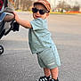 child, toddler, baby, sunglasses, cap, hat_with_text, car, bumper, parking_lot, pavement, shorts, adidas, sandals, smile, standing, leaning, outdoor, casual_clothing, portrait, accessory