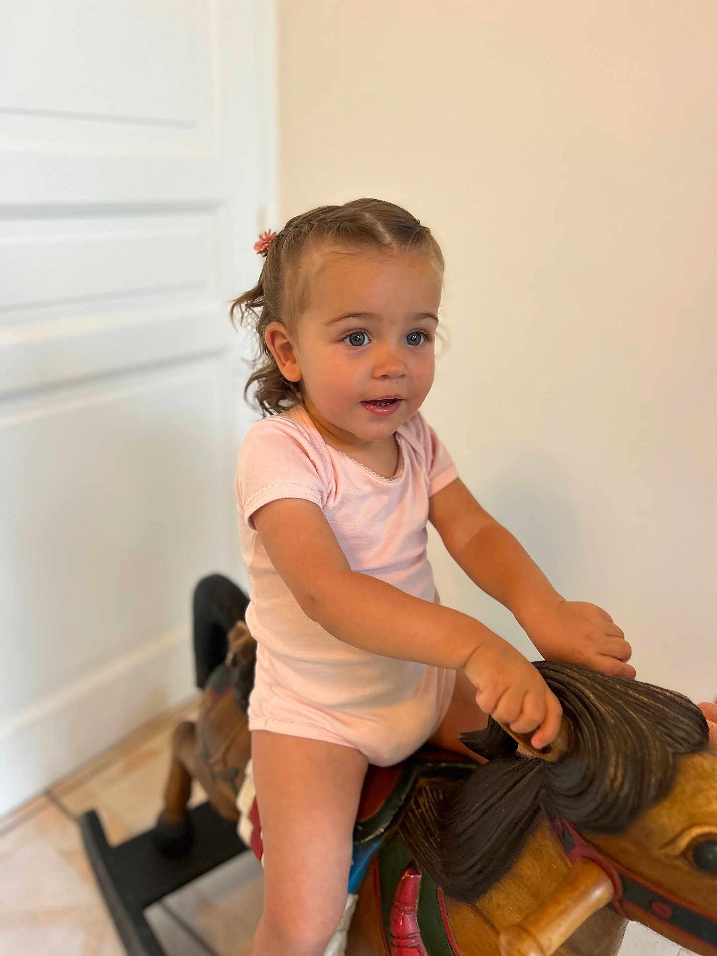 Elena a rejoint le concours — aidez-le/la à gagner de superbes lots ! toddler, child, indoor, rocking_horse, wooden_toy, braided_hair, pink_clothing, floor, door, play, young_child, curious_expression, toy, furniture, childhood, person, portrait, hands, smile, happy