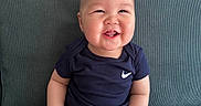 Alim is registered to the contest to win money with this photo: baby, smiling, sitting, onesie, blue_clothing, couch, happy, cute, infant, face, child, indoors, cheerful, plump, portrait, skin, furniture, young_child, tooth, hands