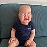 baby, smiling, sitting, onesie, blue_clothing, couch, happy, cute, infant, face, child, indoors, cheerful, plump, portrait, skin, furniture, young_child, tooth, hands