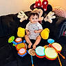 baby, child, toy, drum, plush, minnie_mouse, couch, black_couch, smile, indoor, happy, childrens_toy, colorful, playtime, cute, sitting, person, living_room, soft_toy, infant
