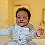 Rukudzo Wesley is registered to the contest to win money with this photo: baby, child, smiling, sitting, indoors, cozy_clothing, fuzzy_outfit, bed, happy, cute, person, infant, portrait, warm_lighting, home, soft_texture, hands, feet, face, curly_hair