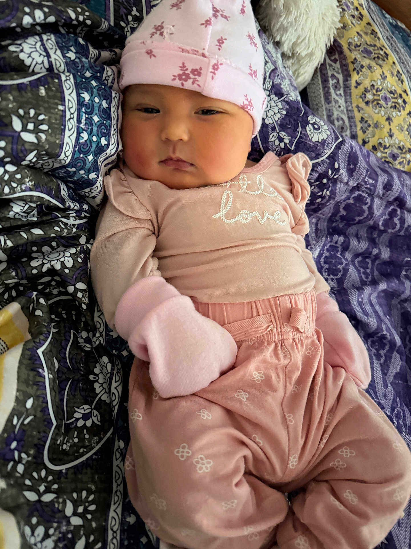 Jasmine is registered to the contest to win money with this photo: baby, infant, pink_clothing, mittens, hat, blanket, pattern, face, person, cute, child, sleepwear, fashion, portrait, lying_down, soft_texture, home, cozy, newborn, expression